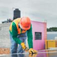 A solar technician working outdoors installing photovoltaic panels with safety gear.