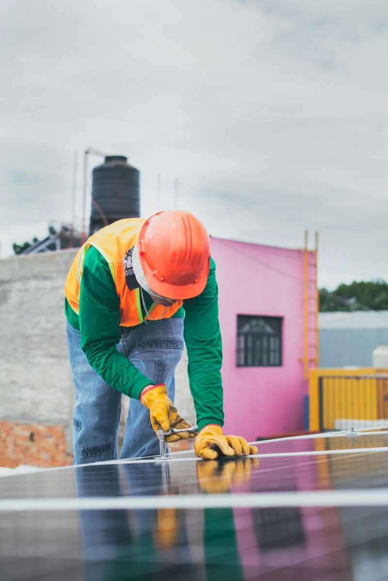 Photo by Los Muertos Crew A solar technician working outdoors installing photovoltaic panels with safety gear.