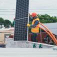 A technician in safety gear installs a solar panel on a rooftop, promoting renewable energy.