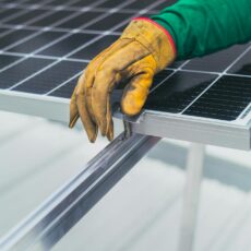 Close-up of a worker's hand in protective glove installing a solar panel.