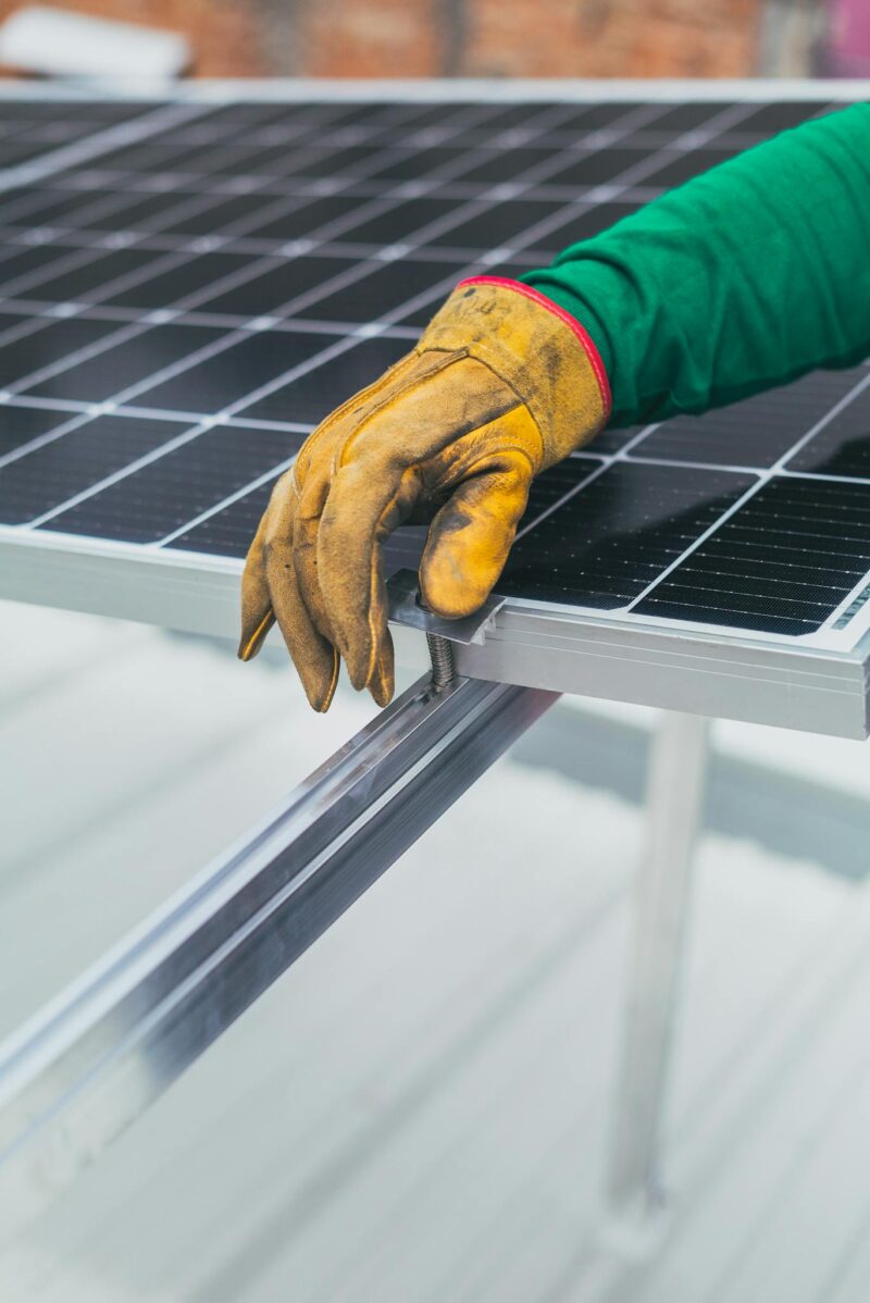 Photo by Los Muertos Crew Close-up of a worker's hand in protective glove installing a solar panel.