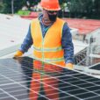 Technician in protective gear installing solar panels on a sunny day.