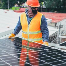 Technician in protective gear installing solar panels on a sunny day.