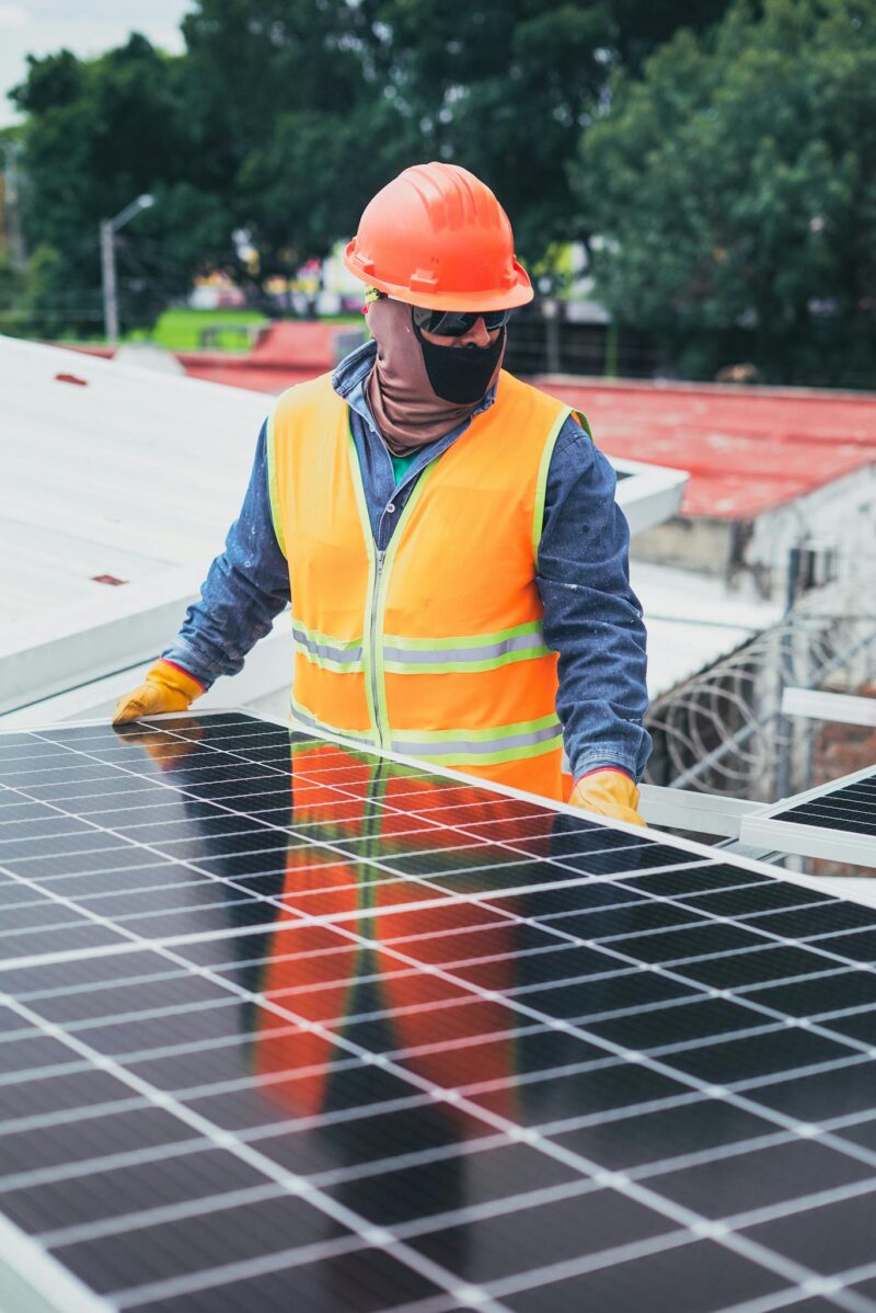 Photo by Los Muertos Crew Technician in protective gear installing solar panels on a sunny day.