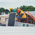 Two workers in safety gear installing solar panels on a rooftop for sustainable energy.