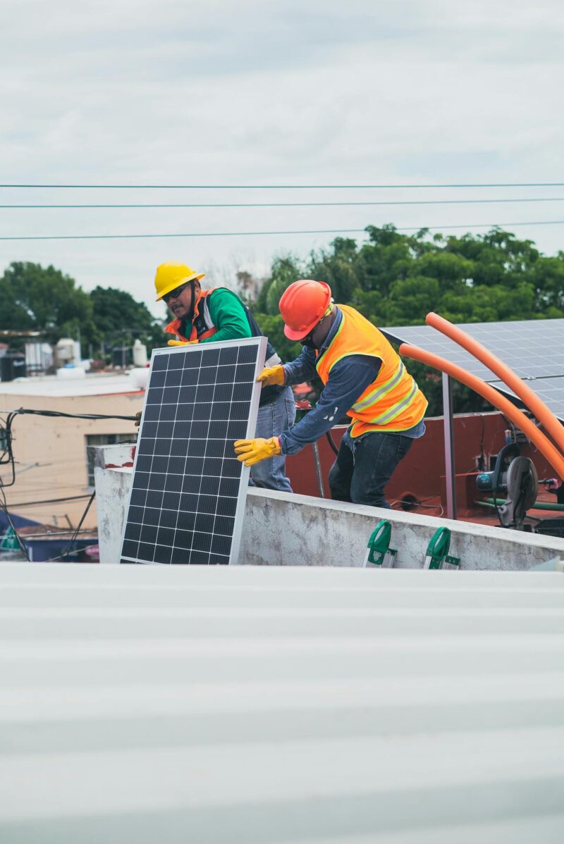 Photo by Los Muertos Crew Two workers in safety gear installing solar panels on a rooftop for sustainable energy.